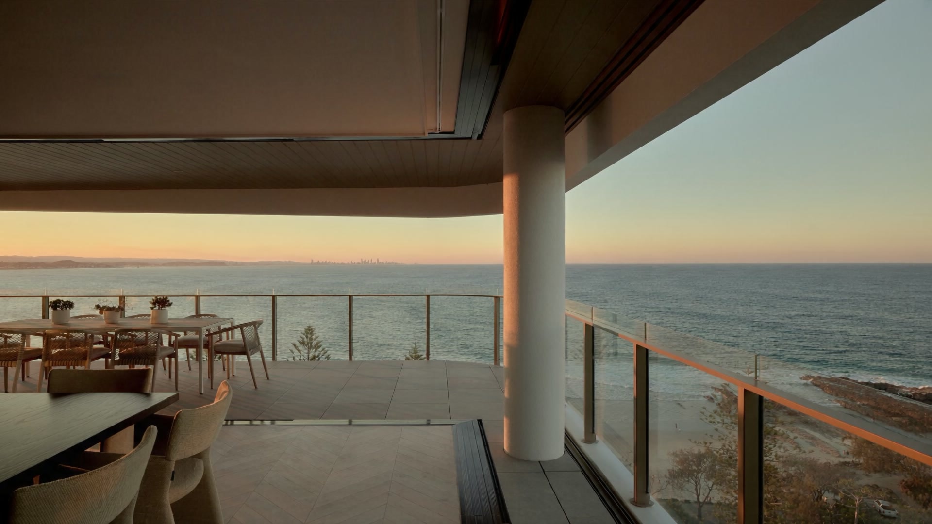 Flow Residences: an apartment terrace at evening, dining table set, the ocean and the Surfers Paradise skyline beyond the glass balustrade